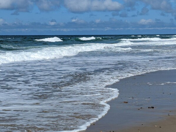 Una playa con olas, cielo despejado y orilla arenosa.