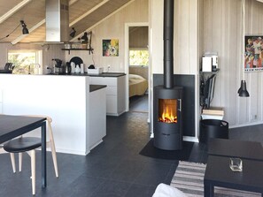 A modern kitchen with a central island, a black wood-burning stove, and a dining area with a table and chairs.