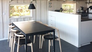 A modern kitchen with a central island, a dining area with a table and chairs, and a view through the window.