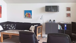 A living room with a black sofa, a wooden coffee table, a floor lamp, and a bookshelf. - 8 Person Holiday Home in Egernsund (Broager)