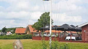 A flagpole with multiple flags, a building with a red roof, and outdoor seating under umbrellas. - 8 Person Holiday Home in Egernsund (Broager)