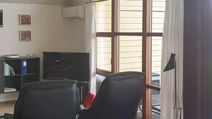 A room with two black office chairs, a bookshelf with books, a flat-screen TV, and a window with blinds. - 8 Person Holiday Home in Egernsund (Broager)