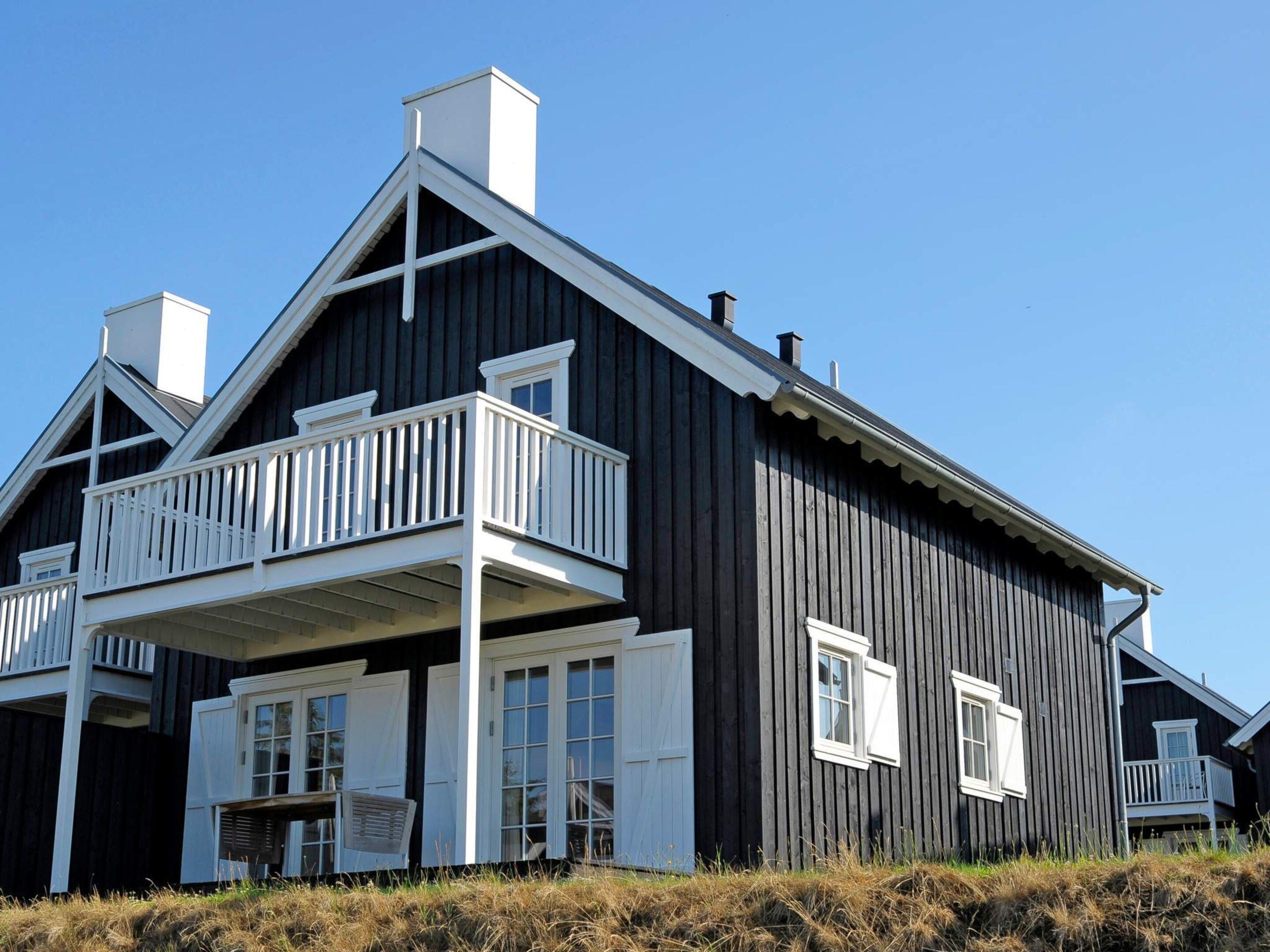 Une grande maison en bois sombre, dotée d’un balcon et de nombreuses fenêtres.