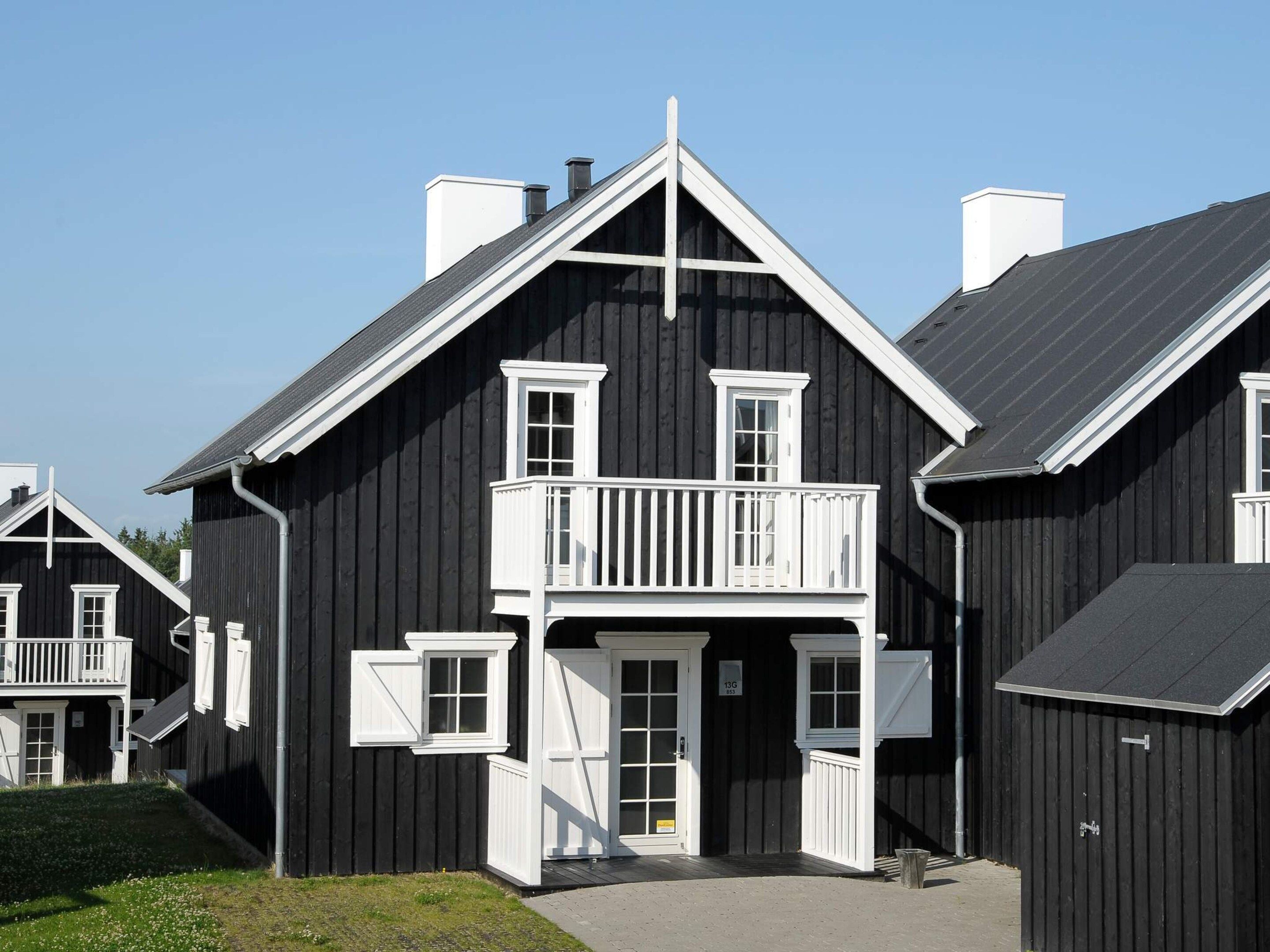 Un bâtiment en bois noir doté d’un balcon et d’une porte portant l’inscription « 13G ».