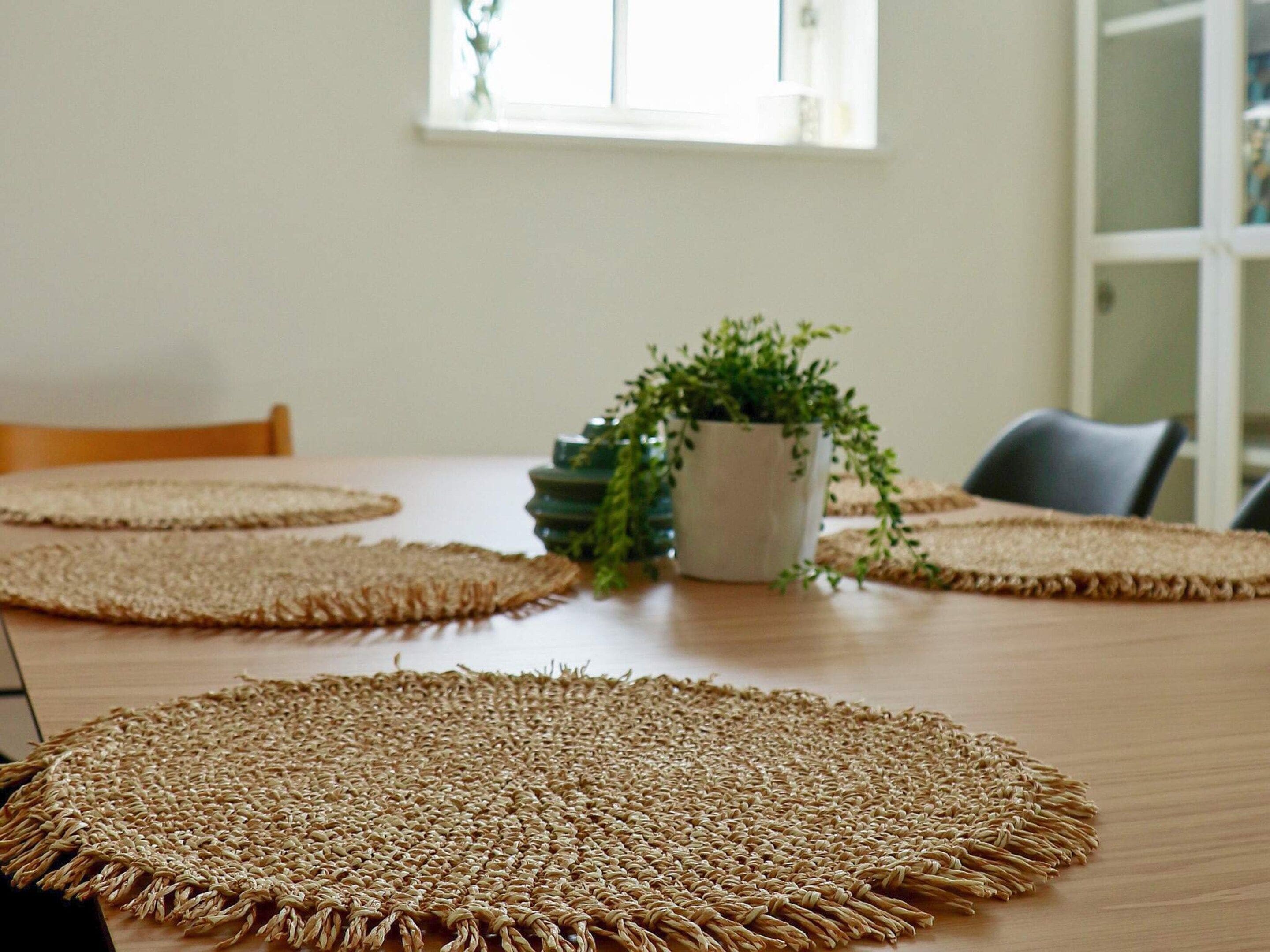 A dining table with four woven placemats and a potted plant.