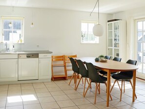 A modern kitchen with white cabinets, a dishwasher, and a dining area with a wooden table and chairs. - 4 Star Holiday Home in Gjern (Gjern)