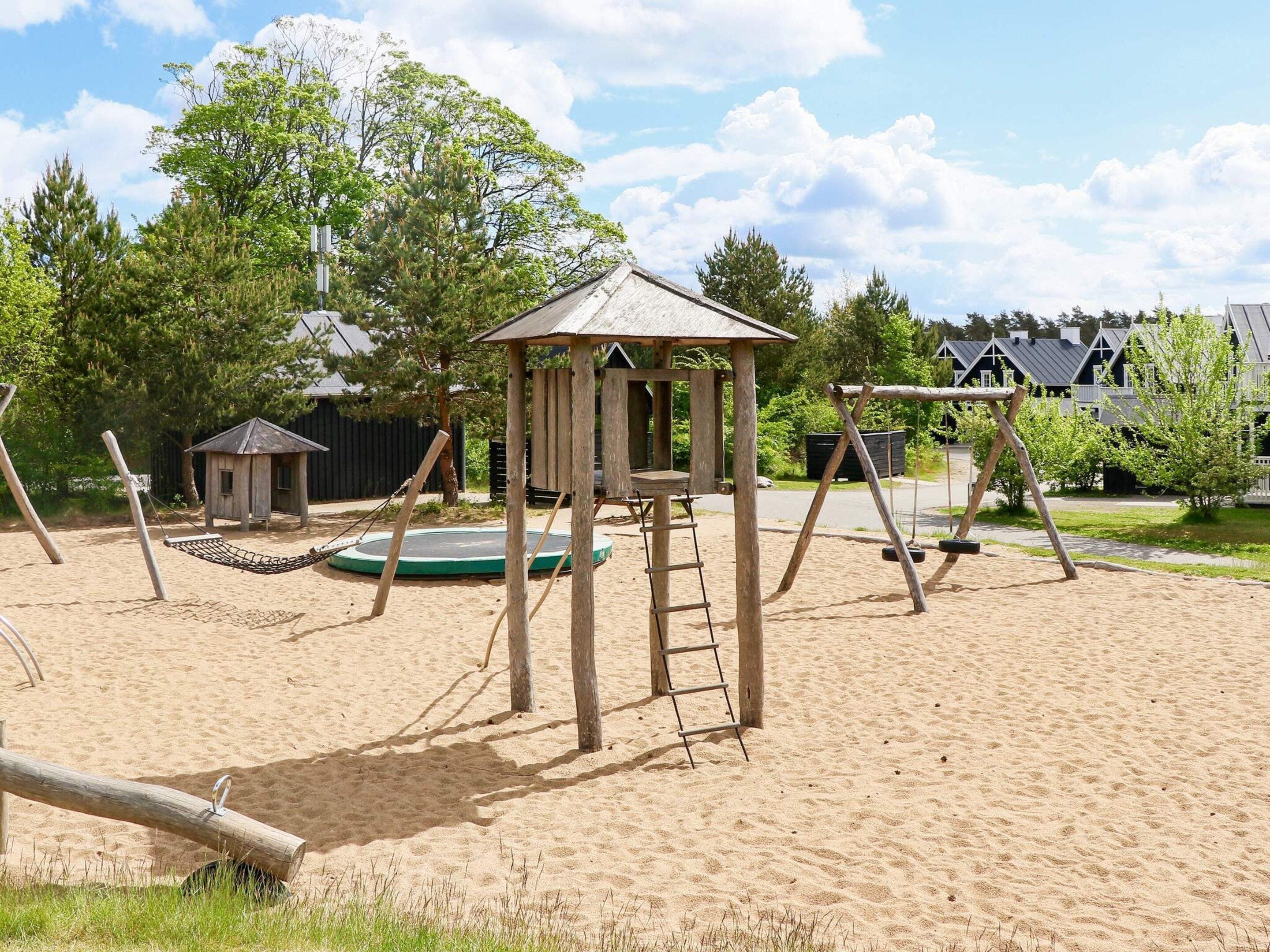 Une aire de jeux avec une balançoire, une petite structure en bois et un trampoline.