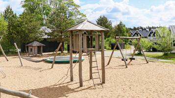 A playground with a swing set, a small wooden structure, and a trampoline.