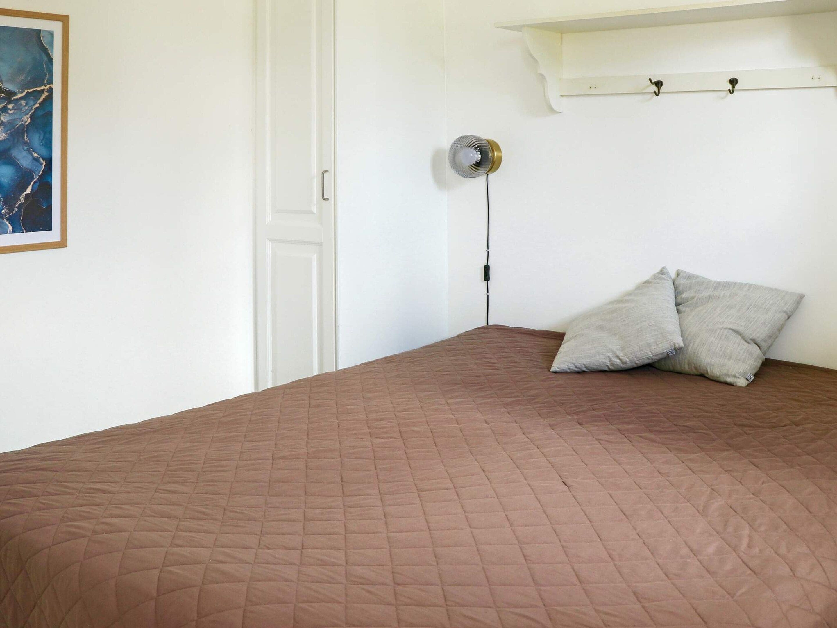 Un dormitorio con colcha marrón acolchada, una puerta blanca, un ventilador de pared y una repisa con ganchos.