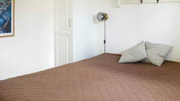 Un dormitorio con colcha marrón acolchada, una puerta blanca, un ventilador de pared y una repisa con ganchos.