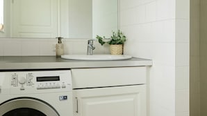 Un baño moderno con lavamanos blanco, un espejo, lavadora y una pequeña planta en maceta.