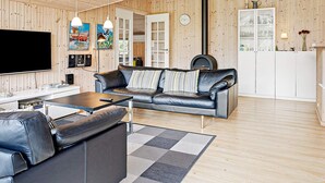 A modern living room with a leather sofa, a flat-screen TV, wooden walls, and a large window.
