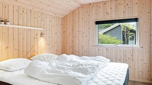 A bedroom with a wooden paneled wall, a bed with white bedding, a bedside lamp, and a window with a view of greenery.