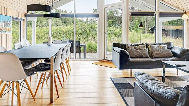 A modern interior with a dining area, a sofa, and a view of greenery.