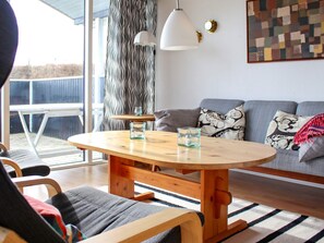 A modern living room with a round wooden table, two chairs, a sofa, and a large window with a view.