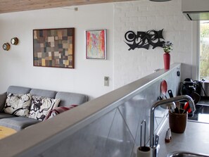 A modern kitchen with a stainless steel countertop, a sink, and various utensils. There is a gray sofa with patterned cushions in the living area. - 4 Person Holiday Home in Broager (Broager)