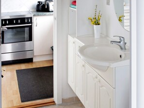 A modern kitchen with stainless steel appliances, a white sink, and a small vase with yellow flowers.