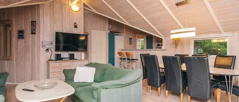 Un salon chaleureux avec un canapé vert, une table à manger avec des chaises, un téléviseur et des murs en bois.