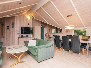 A cozy living area with a green sofa, a dining table with chairs, a TV, and wooden walls. - Pleasing Holiday Home in Ebeltoft near Sea (Ebeltoft)