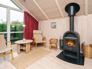 A cozy room with a wood-burning stove, wicker chairs, a round table, and a view through large windows.