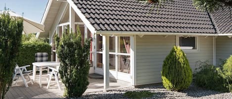 Une maison avec un toit en pente, une véranda et un patio aménagé avec du mobilier d’extérieur.
