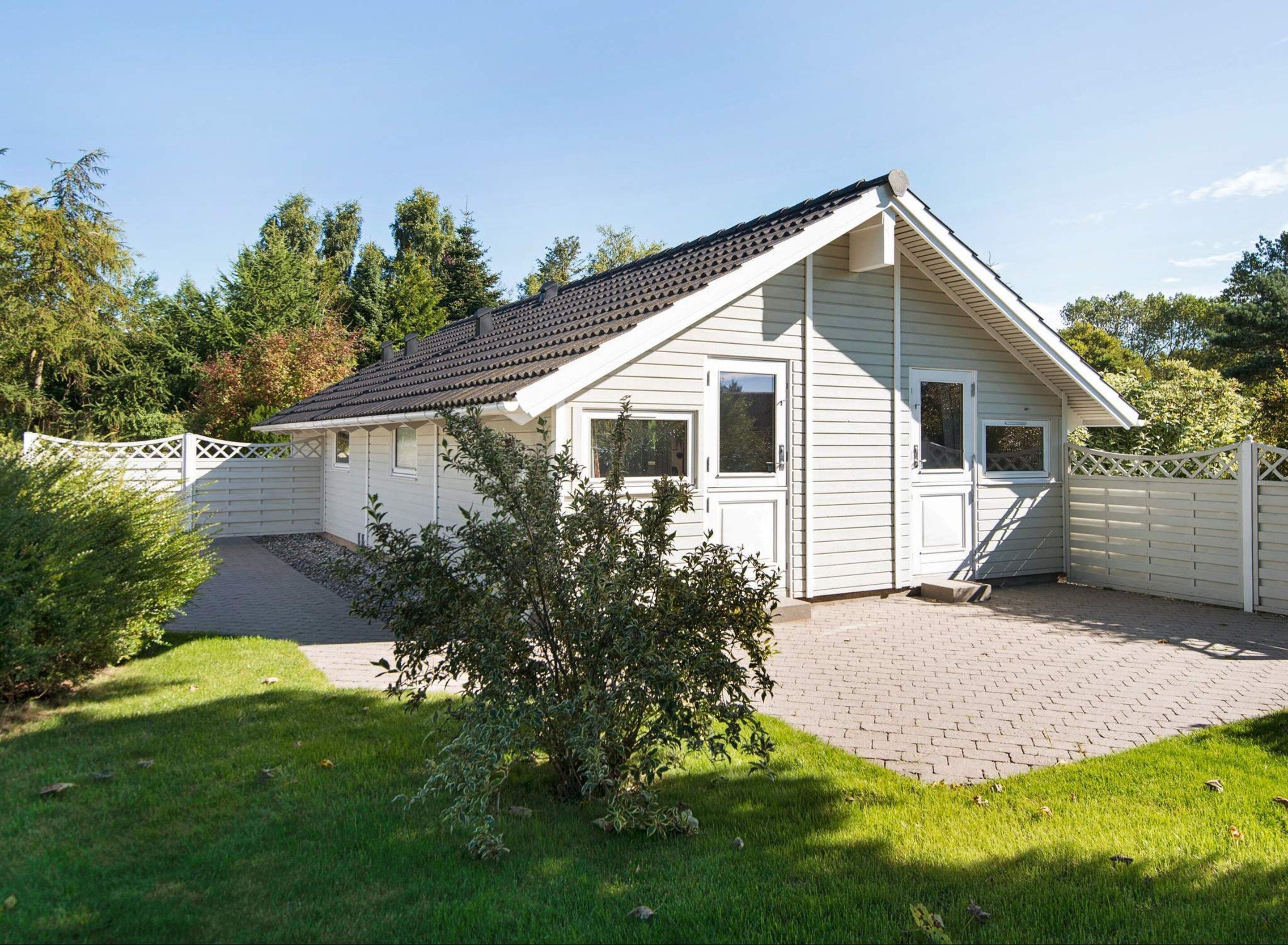Ein eingeschossiges Haus mit geneigtem Dach, einer Veranda und einem eingezäunten Vorgarten.