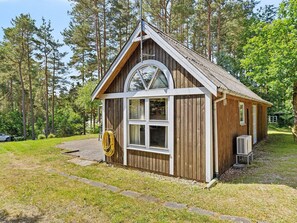Une petite cabane en bois, dotĂ©e dâun toit Ă deux versants, dâune grande fenĂȘtre et dâun tuyau dâarrosage enroulĂ© contre le mur.