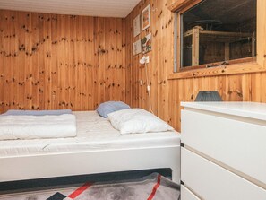 A room with wooden panel walls, a bed with white bedding, a desk with a chair, and a window.