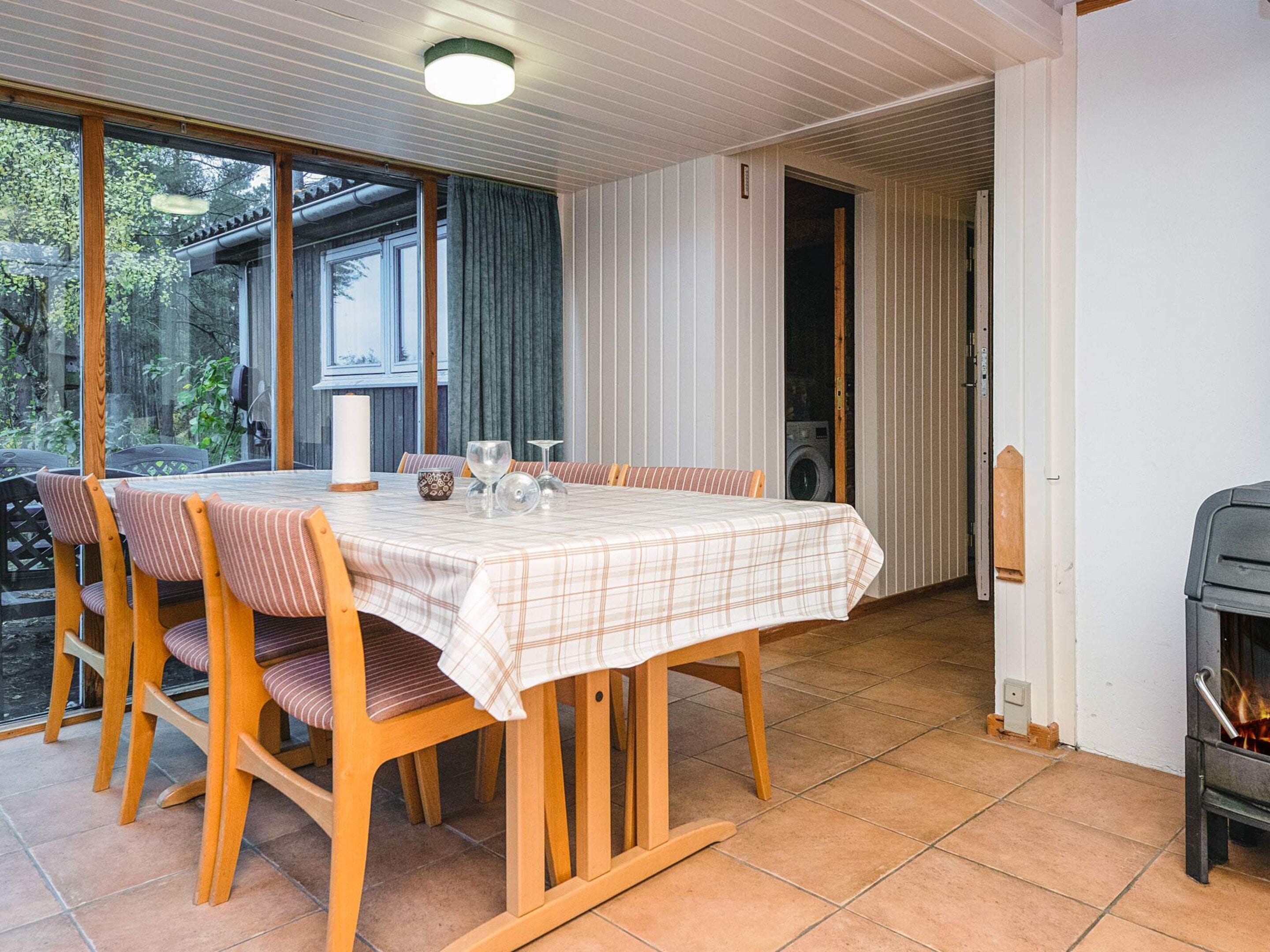 Ein Essbereich mit einem Tisch für vier Personen, Holzsesseln, einem Fenster mit Vorhängen und Blick auf Grünfläche.