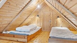 Camera mansardata in legno con due letti, una porta in legno e un soffitto spiovente.