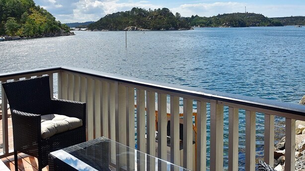A deck with wicker furniture and a glass table overlooking a body of water. - 4 Star Holiday Home in Urangsvag (Bomlo)