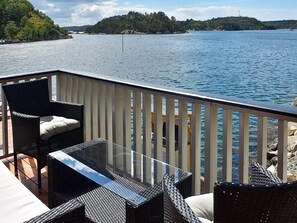 Una terraza con mobiliario de mimbre y una mesa de vidrio con vista a un cuerpo de agua.
