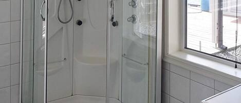 A corner shower enclosure with a glass door, a window, and a white tiled wall.
