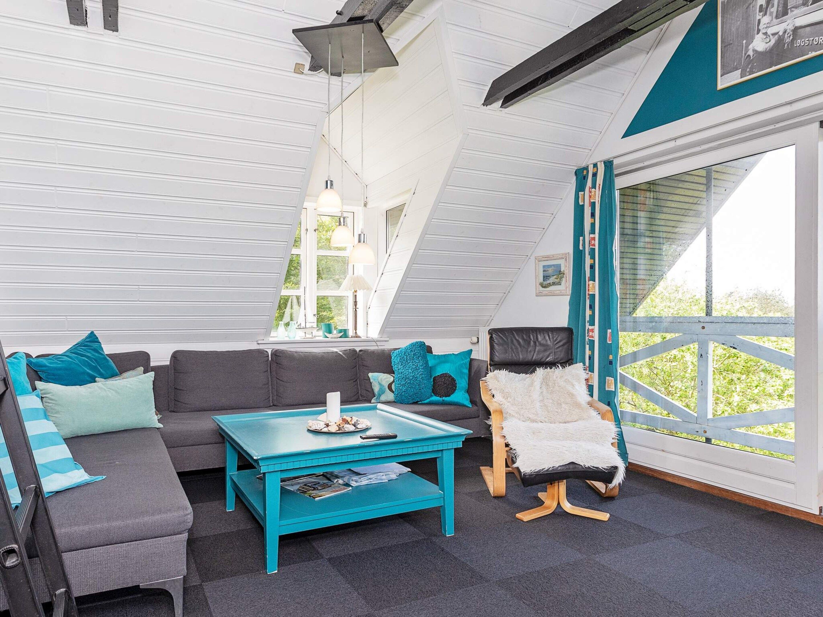 A modern living room with a sofa, a coffee table, and a chair. There is a window with curtains and a view of greenery outside.
