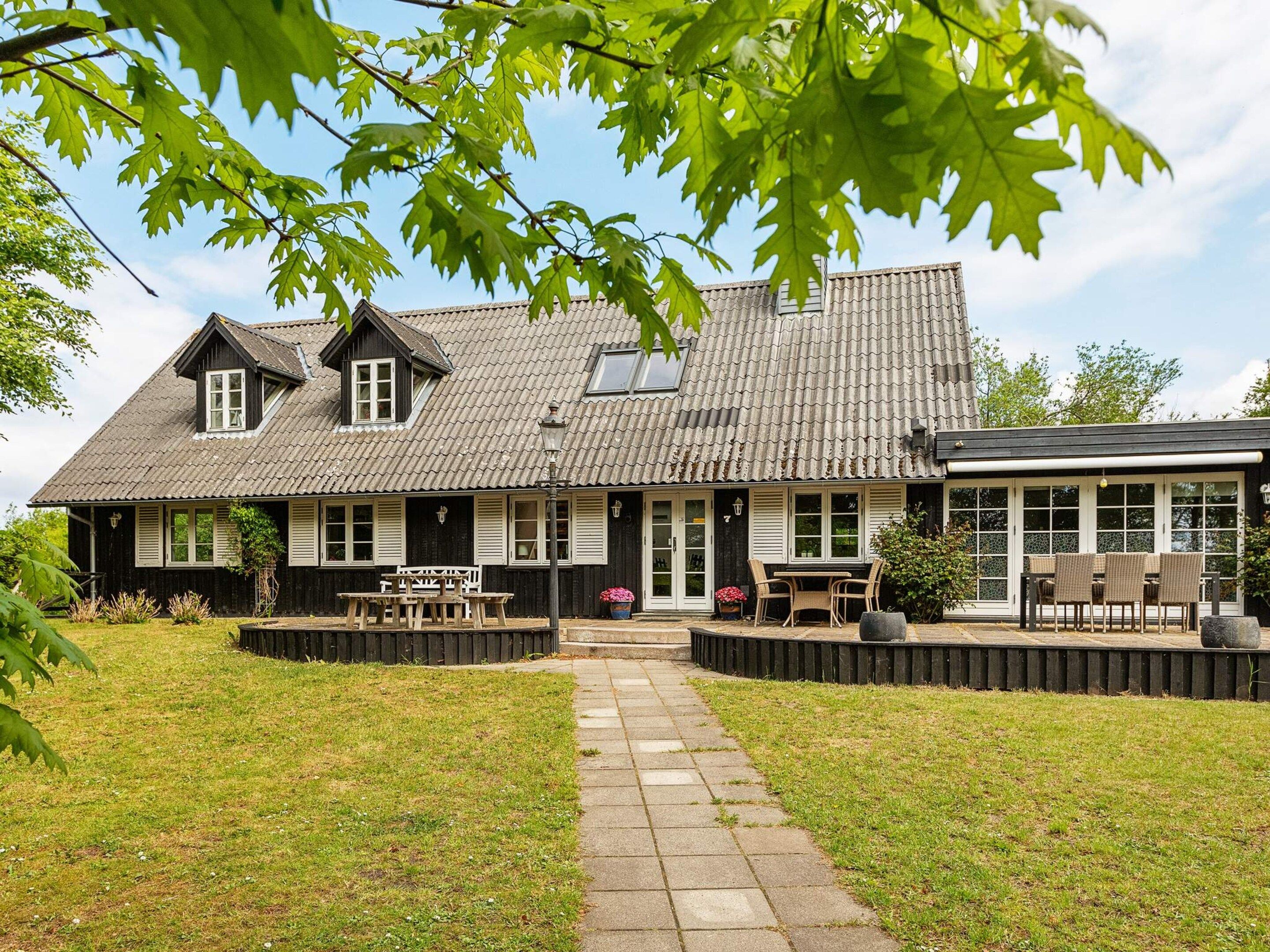 A traditional house with a tiled roof, a front porch with seating, and a pathway leading to the entrance.