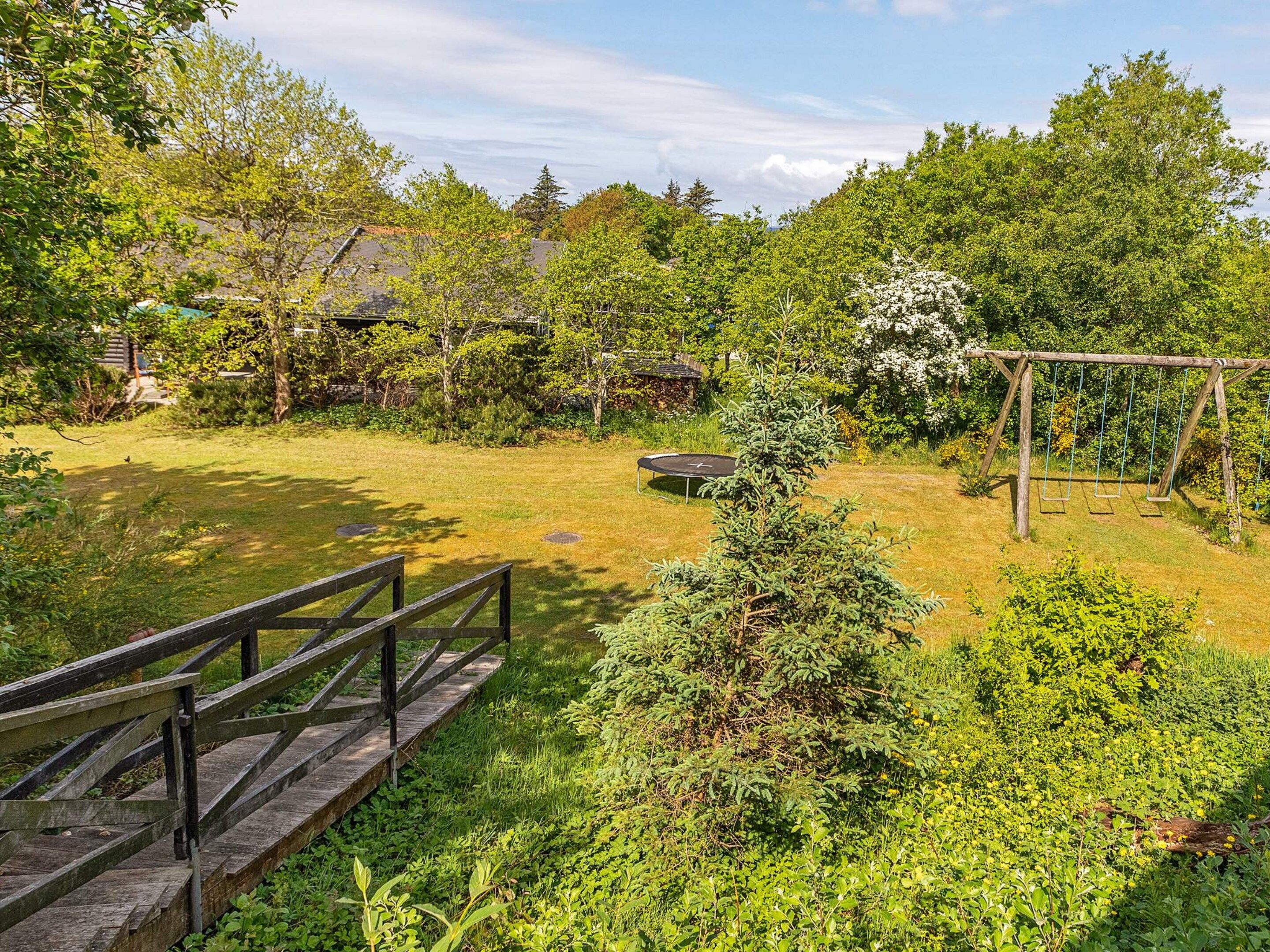 A wooden deck with a metal railing, surrounded by lush greenery and a small pond.