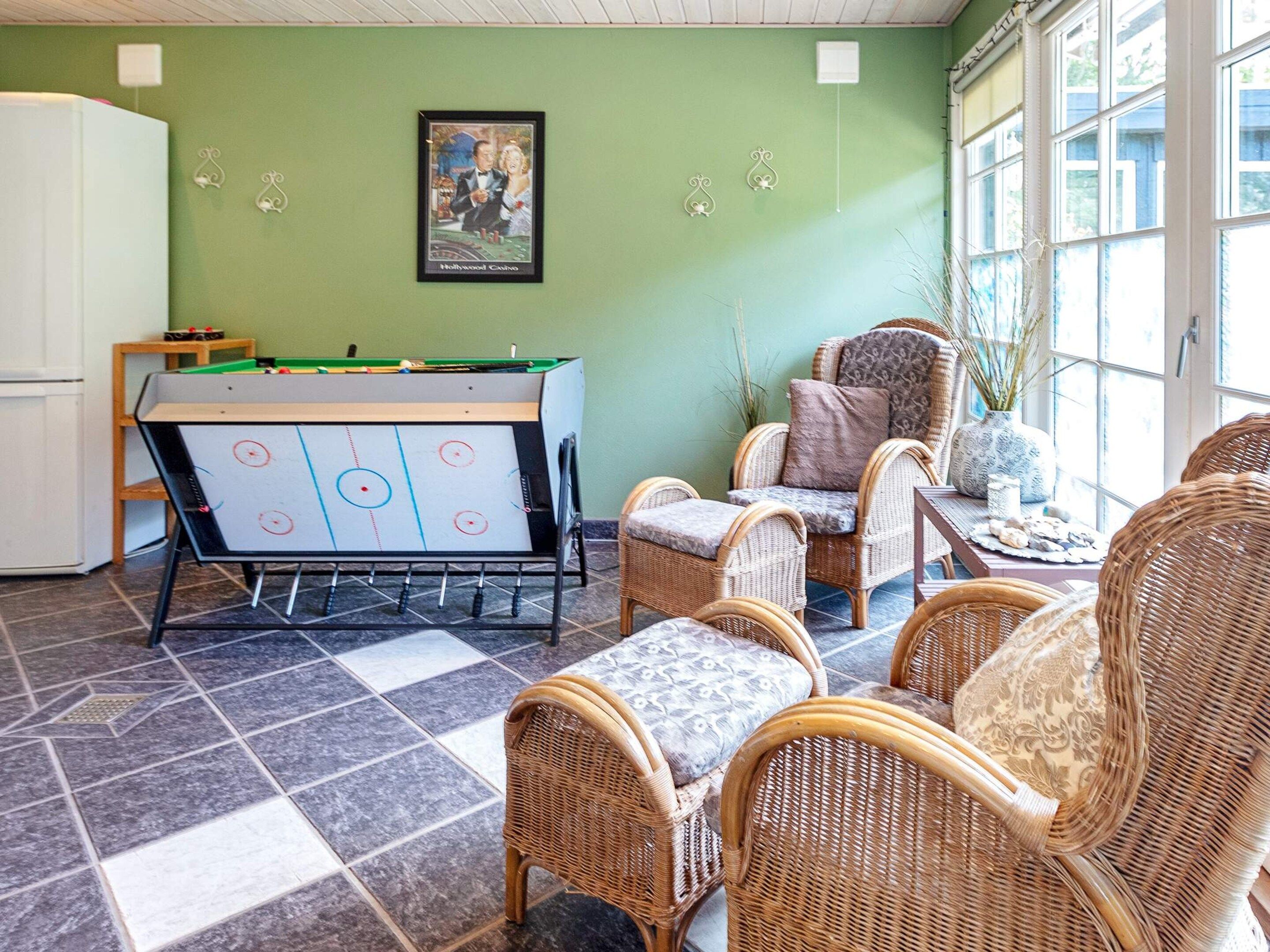 A room with a foosball table, wicker chairs, and a large window.