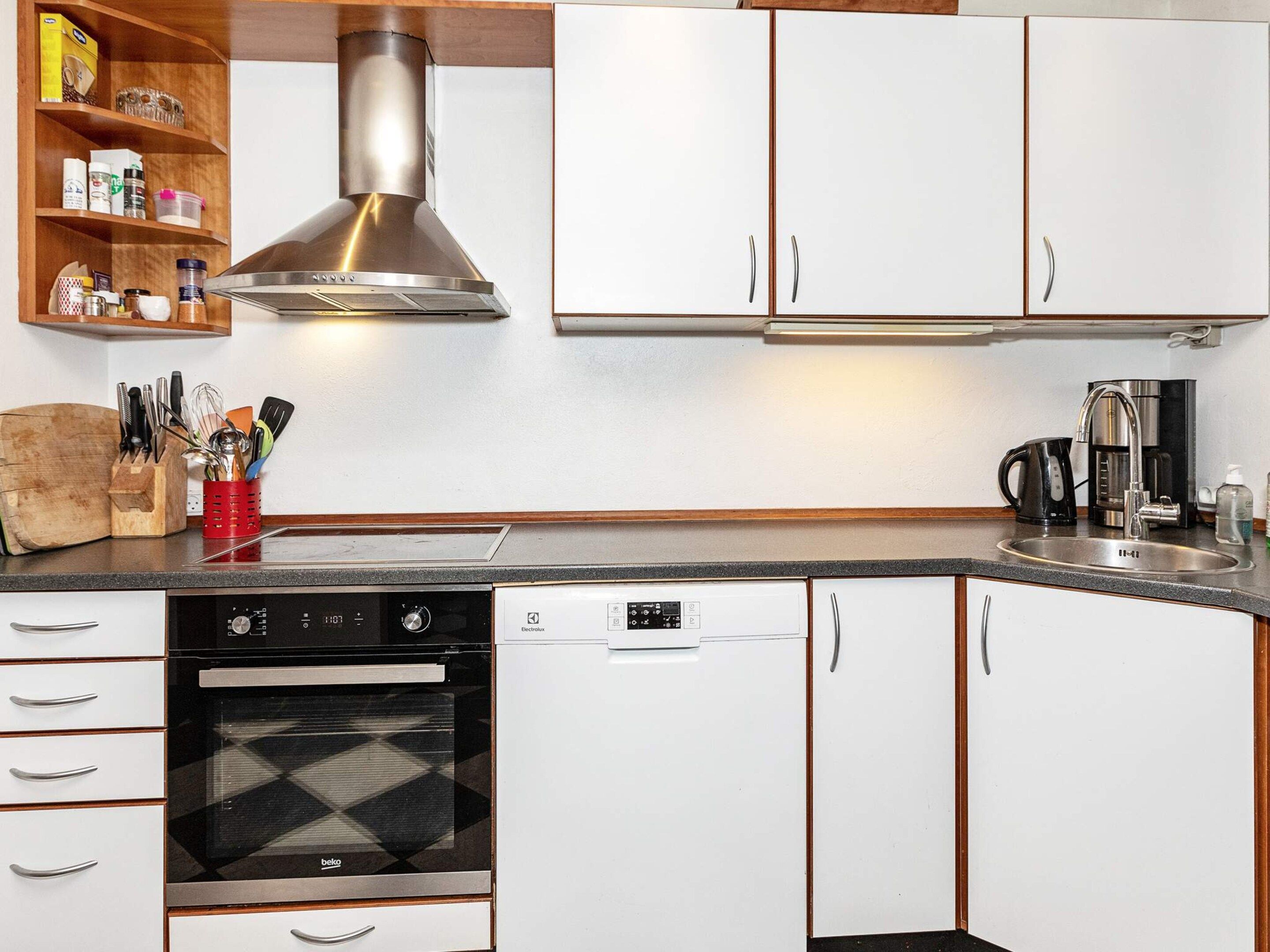 A kitchen with white cabinets, a stainless steel range hood, a dishwasher, and a coffee maker.