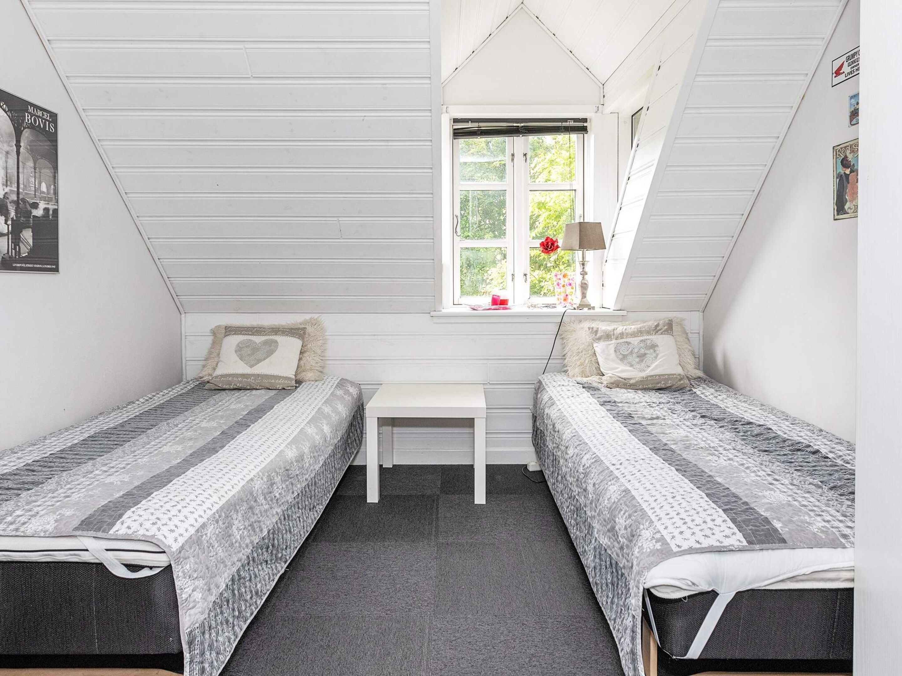 A bedroom with two single beds, a small table, and a window with a view of greenery.