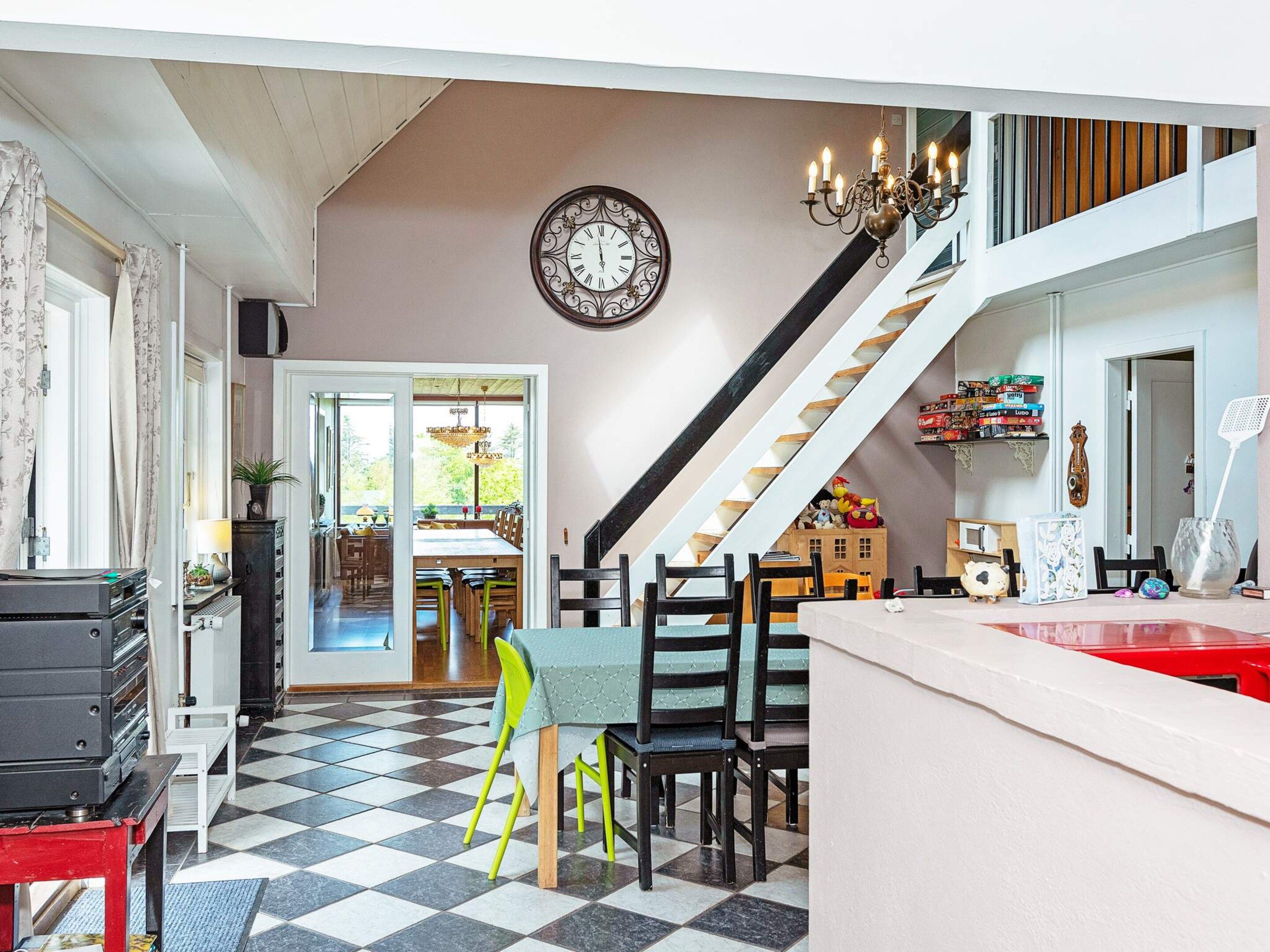 A dining area with a checkered floor, a staircase, and a clock on the wall.