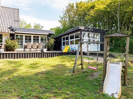 Una propiedad residencial con terraza, mobiliario exterior y zona de juegos que incluye un tobogán y columpios.