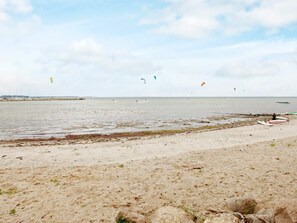 A beach with a sandy shore, a pier in the distance, and several kites in the sky. - Holiday Home in Gelting (Gelting)