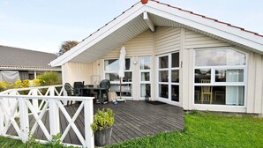 Une maison à deux étages avec un patio couvert, une terrasse clôturée et une cour gazonnée.