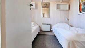 A small, compact room with two beds, a radiator, a mirror, and a white door. - Holiday Home in Gelting (Gelting)