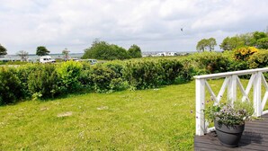 A grassy deck with a white railing, a potted plant, and a view of a marina with boats and a distant shoreline. - Holiday Home in Gelting (Gelting)