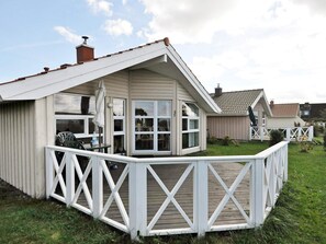 Ett envåningshus med vit fasad, en täckt veranda med ett vitt räcke och en liten uteplats.