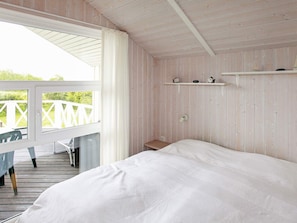 A bedroom with a bed, a desk, and a chair. There is a balcony with a railing and a view of greenery. - Holiday Home in Gelting (Gelting)