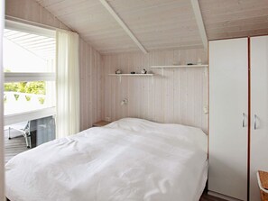 Quarto com cama, guarda-roupa, prateleira com objetos decorativos e janela com cortinas.