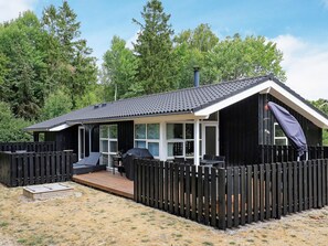 En stuga med en veranda, en möblerad uteplats under tak och en inhägnad trädgård.