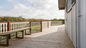 A wooden deck with benches, a white building with windows, and a hedge in the background. - 5 Person Holiday Home in Ebeltoft (Ebeltoft)